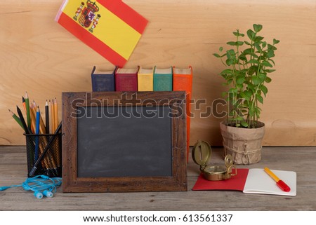 Learning Spanish language concept - blank blackboard, flag of the Spain, books, pencils, compass on wooden background