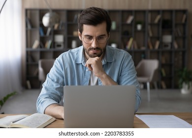 Learning Subject Online. Serious Millennial Bearded Male In Glasses Watch Elearning Training Course Webinar At Laptop Screen From Home. Pensive Young Man Get Remote Education Study Video Lesson On Pc