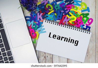 LEARNING text on notebook with laptop and piles of alphabet on wooden table. 