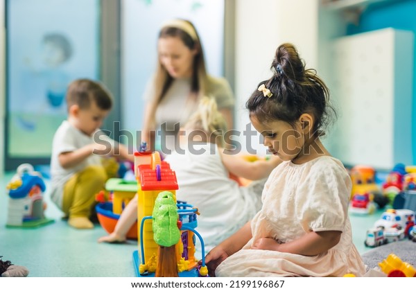 Learning through play at the nursery school. Toddler\
little girl and the teacher playing with colorful plastic\
playhouses, building blocks, cars and boats. Imagination,\
creativity, fine motor\
and