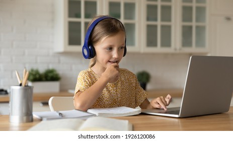 Learning time. Interested little kid schoolgirl in headset sit at home desk watch education video lesson. Curious small school age girl think on teacher question select correct answer on laptop screen