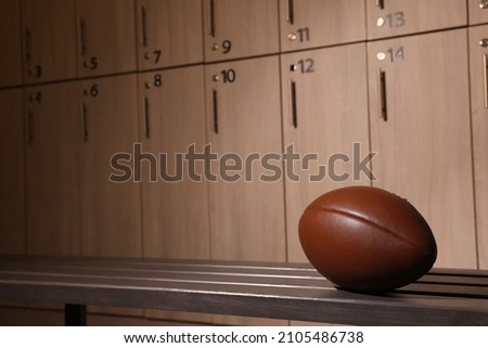 Leather American football ball on wooden bench in locker room. Space for text