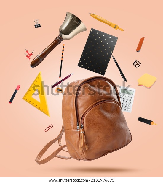 Leather backpack, school bell and different\
stationery flying on beige\
background