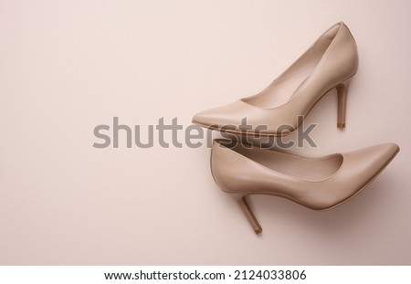 Leather beige high heel shoes on a beige background, top view 
