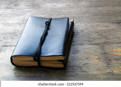 A leather bound journal sits on a table outside with a cord wrapped around the pages to keep place in book.