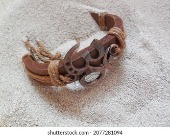 A leather bracelet with a metal emblem of the mantra om, aum, a symbol of truth and infinity. The decoration (the property of the author of the photo) lies on the sand.