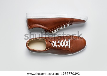 Leather brown men's sneakers with white laces and rubber soles on gray background. Flat lay top view. Men's sports casual shoes. Fashionable sneakers. Male fashion, hipster footwear Minimal background