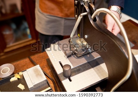 Leather crafting with iron press machine. Craftsman hands working at leather engraving machine. Working process of making leather wallet in the leather workshop, close-up