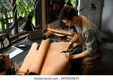 Leather craftsman cutting a large piece of leather with scissors on a workbench. Handicraft business concept. - Powered by Shutterstock