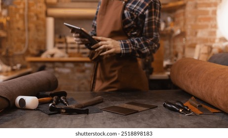 Leather craftsman uses computer tablet for communications on atelier workshop. Concept technology in DIY business banner. - Powered by Shutterstock