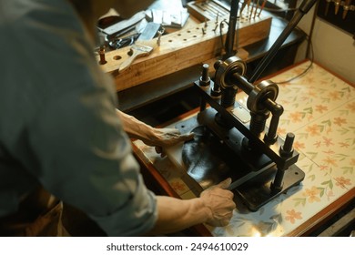 Leather craftsman using a manual rolling machine working on a leather project in his local workshop. - Powered by Shutterstock