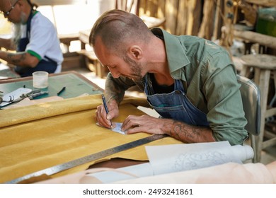 Leather craftsman using a pencil drawing draft design on the yellow leather in the workshop. - Powered by Shutterstock