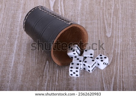 Leather dice cup lies on the wooden table and six white dice fall out