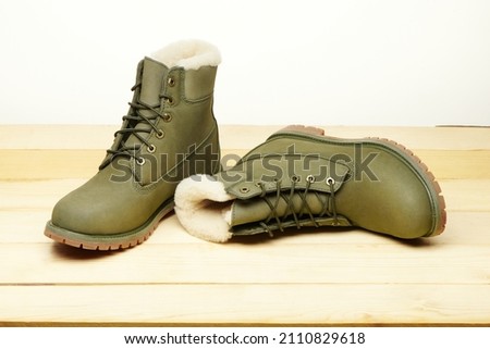 Leather green waterproof boots with white fur for winter hiking wooden table. Winter shoes. Warm shoes with fur. Fashion, trendy footwear. Close up view.