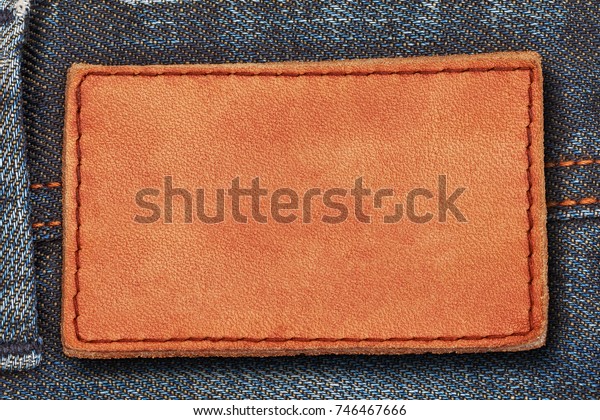 Leather label on denim jean background, close up.\
Brown leather tag, double seams strap on dark blue denim jeans.\
Leather frame with brown\
seam