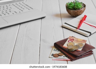 Leather man's open wallet with euro banknotes, coins on a white wooden table, close-up, selective focus, shallow depth of field. Planning purchases and expenses, laptop and notepad next to the table