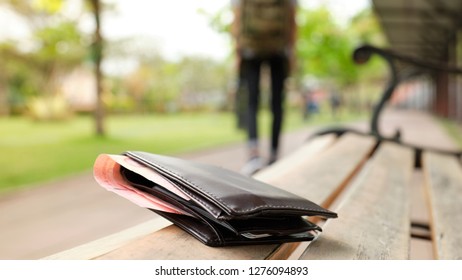 Leather purse with a money lying on the park bench while tourists are walking away. - image - Shutterstock ID 1276094893