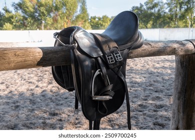 Leather saddle with stirrups for show jumping race. Saddle for riding horse. Horse saddle on rural fence. Equestrian sport event background - Powered by Shutterstock