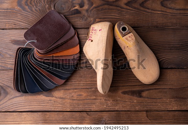 Leather\
samples for shoes and wooden shoe last on dark wooden table.\
Designer furniture clothes. Shoe maker\
workspace.
