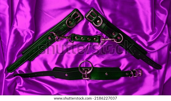 Leather\
straps handcuffs, collar on a purple satin\
sheet.