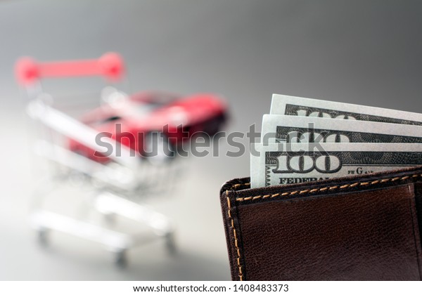 leather wallet with\
dollars blurred red car shopping trolley on the background. cheap\
used cars concept