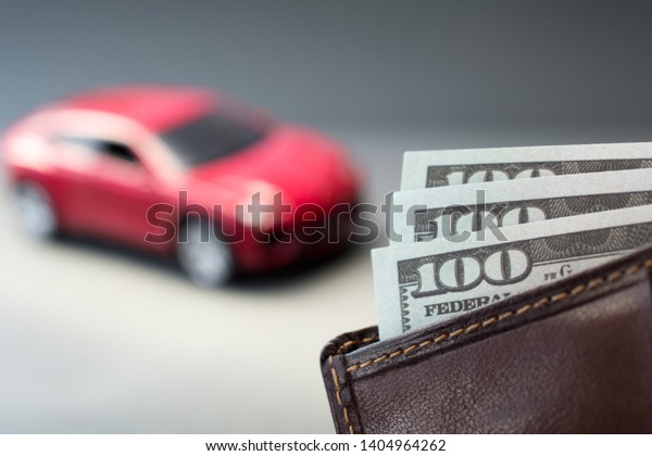 leather wallet with dollars money,\
blurred red car on the background. used cars for sale\
concept