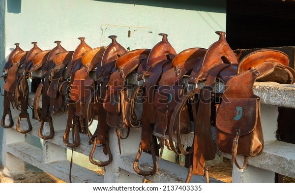 leather western trail saddles with saddle bags and\
horns lined up on white fence in rural Cuba saddle bags marked with\
letters horizontal format shot before horse back riding adventure\
in rural Cuba