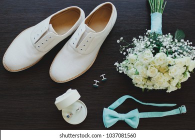 Leather White Groom Wedding Shoes On The Wooden Background In Sun Rays. Rings, Bow Tie And Cufflinks With Elegant Bouquet. Elegant Wedding Details Flat Lay. Tiffany Light Blue Color.