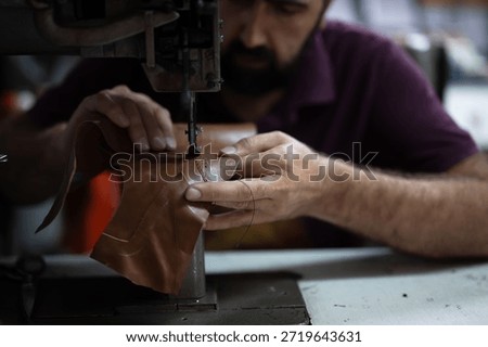 Leather work in progress: skilled craftsman sewing brown leather piece with industrial sewing machine