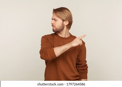Leave me! Portrait of upset vexed man with beard in sweatshirt pointing finger aside, ordering get out and looking resentful, boss dismissing from work, showing exit. indoor studio shot isolated