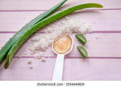 leaves of aloe on a pink background, next to a white spoon with aloe gel and sea salt