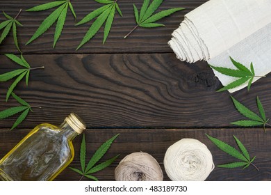 Leaves of cannabis, a bottle of hemp oil and tangles of thread on dark wooden surface. Hemp products. Agricultural technical culture. Top view