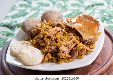 Lechona With Rice, Arepa And Potato On A White Plate And A Background With Plants.