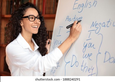 Lecture Concept. Closeup Portrait Of Cheerful Smiling Female Tutor In Spectacles Teaching English Language, Writing Grammar Rules On Whiteboard With Marker, Explaining New Theme To Students