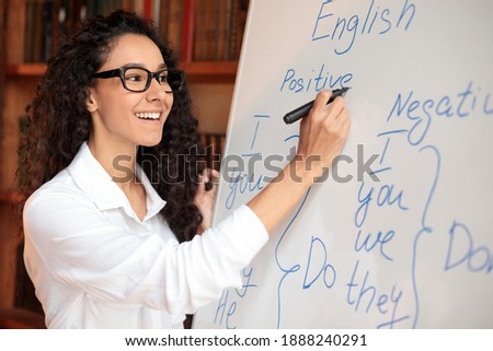 Lecture Concept. Closeup portrait of cheerful smiling female tutor in spectacles teaching English language, writing grammar rules on whiteboard with marker, explaining new theme to students
