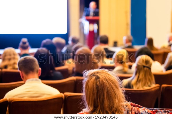 Lecturer In
Front of the White Screen on Stage for the Group of Business People
at a  Conference. Horizontal
Image
