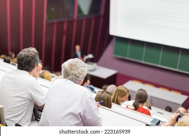 Lecturer At University. Healthcare Expert Giving A Talk To Medical Faculty Professors. Participants Listening To Lecture And Making Notes.