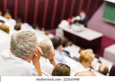 Lecturer At University. Healthcare Expert Giving A Talk To Medical Faculty Professors. Participants Listening To Lecture And Making Notes.