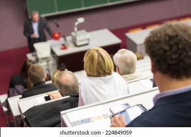 Lecturer At University. Healthcare Expert Giving A Talk To Medical Faculty Professors. Participants Listening To Lecture And Making Notes.