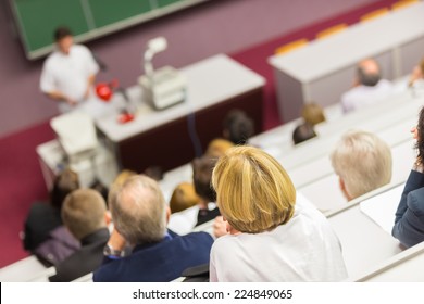 Lecturer At University. Healthcare Expert Giving A Talk To Medical Faculty Professors. Participants Listening To Lecture And Making Notes.