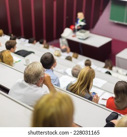 Lecturer At University. Healthcare Expert Giving A Talk To Medical Faculty Professors. Participants Listening To Lecture And Making Notes.