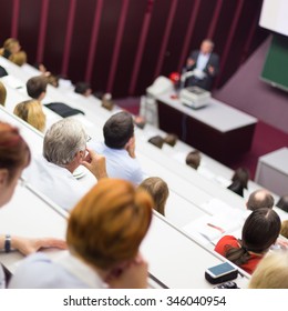 Lecturer At University. Healthcare Expert Giving A Talk To Medical Faculty Professors. Participants Listening To Lecture And Making Notes.