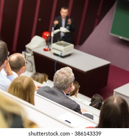 Lecturer At University. Medical Expert Giving A Talk As An Faculty Professor. Participants Listening To Lecture And Making Notes.