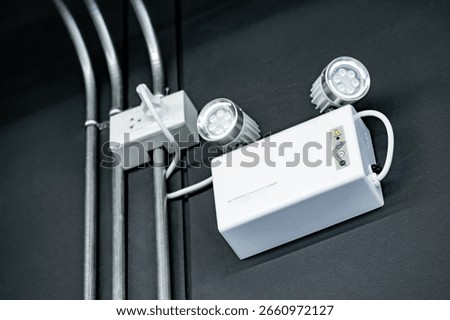 LED Automatic emergency light mounted on black wall in industrial warehouse or factory building. Backup on battery when power outage