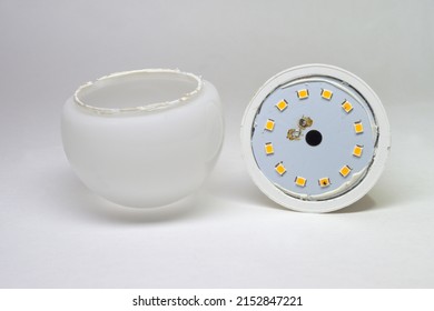 LED bulb disassembled, removed domed white translucent light dispersion optics with silicon sealant at narrow rim. showing inner metal, blue film coated plate with mounted light emitting LEDs array - Shutterstock ID 2152847221