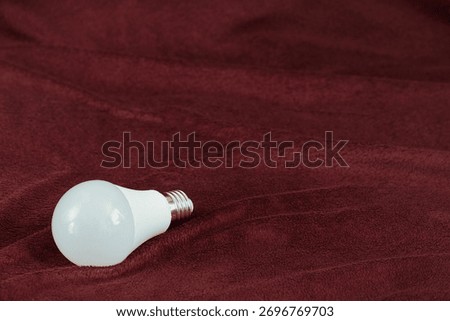 LED bulb with E27 base on soft burgundy fabric with folds. 10-watt energy-saving bulb with neutral light.