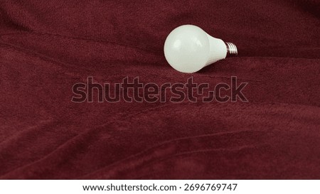 LED bulb with E27 base on soft burgundy fabric with folds. 10-watt energy-saving bulb with neutral light.