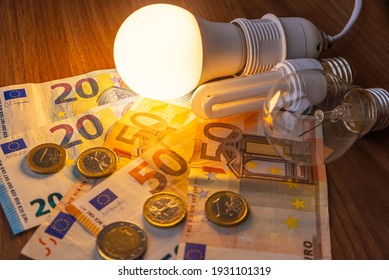 LED bulb on, with fluorescent bulb and incandescent bulb, with bills and coins next to it. Energy costs and evolution of light bulbs.