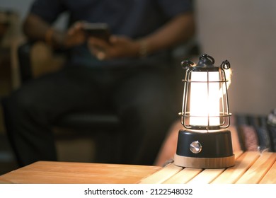 Led camping lamp on the wooden table, Man nice couple having fun on camping with kerosene lamp, sitting on a smartphone.