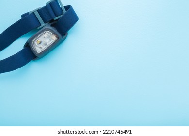 Led Headlamp With Elastic Strap On Light Blue Table Background. Pastel Color. Closeup. Equipment For Work Or Sport Activities In Dark Time. Empty Place For Text.